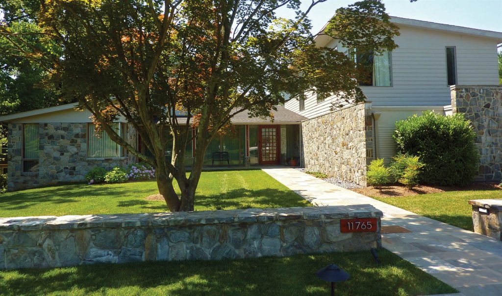 well manicured lawn with stonework fence in front of a residential home