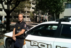 Police officer seated on front of cruiser hood