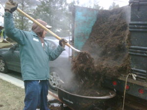 Allentuck employee using a pitchfork to load mulch into a wheelbarrow