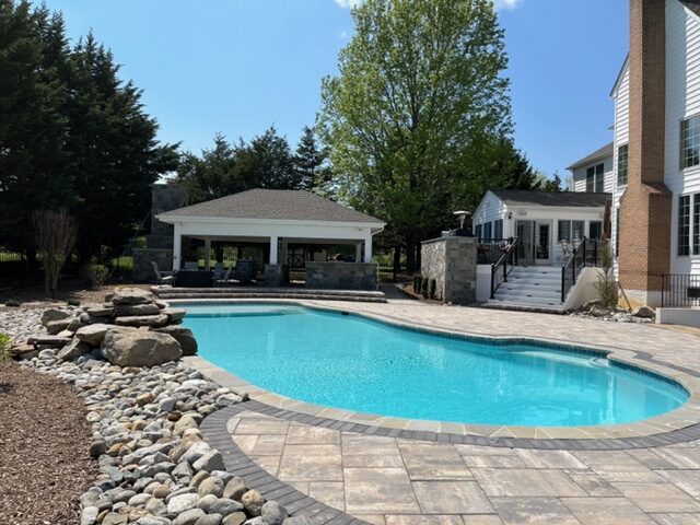 New swimming pool surrounded by rock installation and mulched flowerbeds